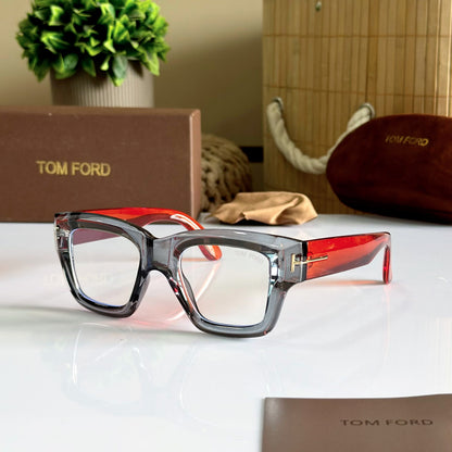 Tom Ford eyeglasses with a translucent smoky gray frame and red acetate temples, displayed on a white surface with the brand's box, case, and cloth in the background.